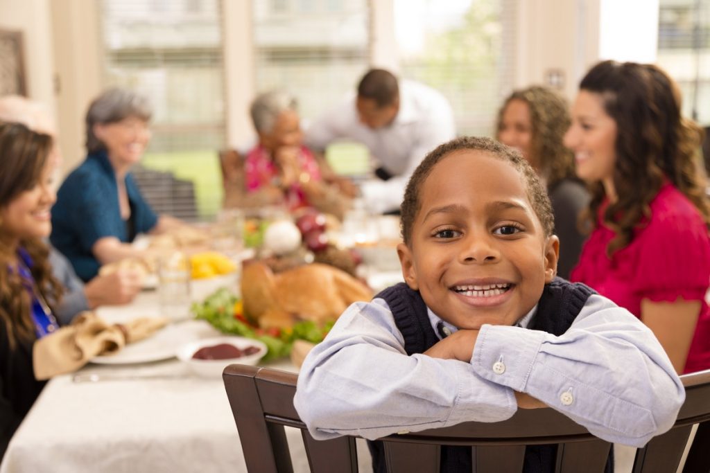 Family and neighbors gather together for Thanksgiving dinner.  Grandson poses for camera.