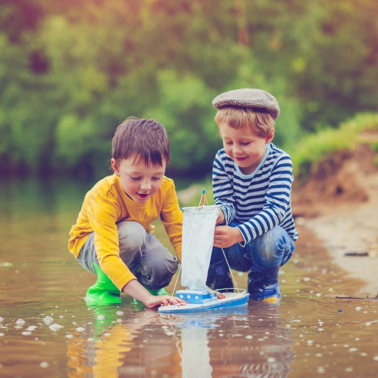 Little boys with their toy ship near a lake in summer