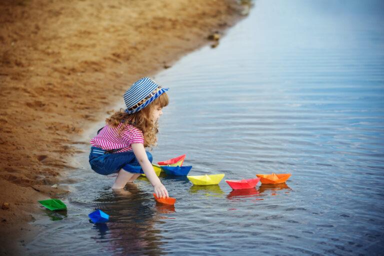 child playing with paper boats in the water