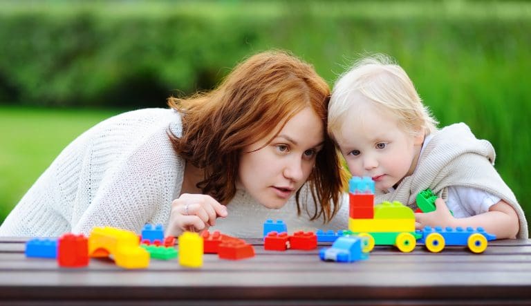 Young woman with his toddler son playing with colorful plastic blocks
