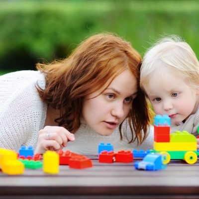 Young woman with his toddler son playing with colorful plastic blocks