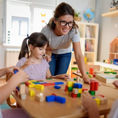 Preschool teacher with children playing with colorful wooden didactic toys at kindergarten