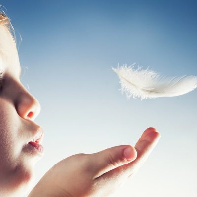 Conceptual close up of a little girl blowing a bird feather away.