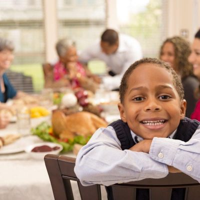 Family and neighbors gather together for Thanksgiving dinner.  Grandson poses for camera.